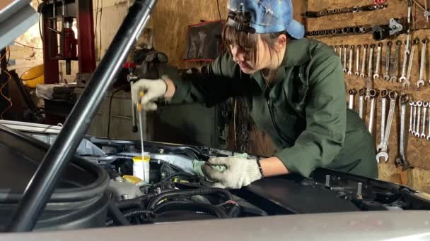 穿着工作服的年轻妇女在汽车加油站工作 负责换油 女机修工检查油位 用抹布擦拭油条的末端 再将其插入室内发动机 — 图库视频影像