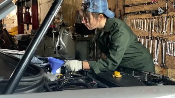 穿着工作服的年轻妇女在汽车加油站工作 负责换油 女机修工将真正的发动机用油倒入室内的油缸 背景下的汽车工具 — 图库视频影像