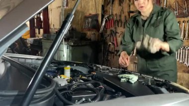Tulumlu genç bir kadın araba tamirhanesinde çalışıyor, araba tamirini tamamlıyor, ellerini içeride bir bezle siliyor. Kadın tamirci motoru ve bileşenleri inceler ve işi bitirir.