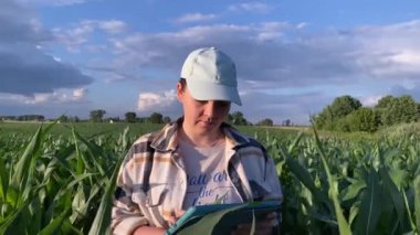 Bir mısır tarlasında dijital tablet kullanarak araştırma yapan genç bir tarım uzmanı. Kadın çiftçi çalışıyor, tarlaya bakıyor. Tarım tarımı keşfi. Dramatik bulutlu gökyüzü arkaplanı