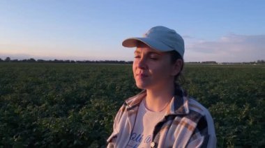 Genç çiftçi kadın altın saatin huzurlu parıltısıyla patates tarlasına bakıyor. Kameraya doğru bakıyor, gerçek bir gülümseme yüzünde pozitif duygular yayıyor. Tarım işgali