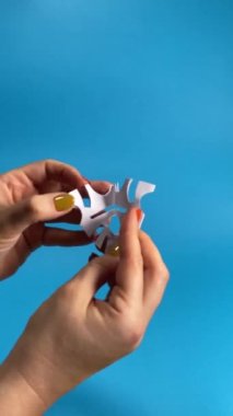 Bayram dekoru, Noel neşesi, kutlama ve canlı mavi bir arka plan karşısında neşeli bir atmosfer. Bir kadın eli kapalı alanda kağıt bir kar tanesinin kapağını açar. Origami gemisi. Dikey video