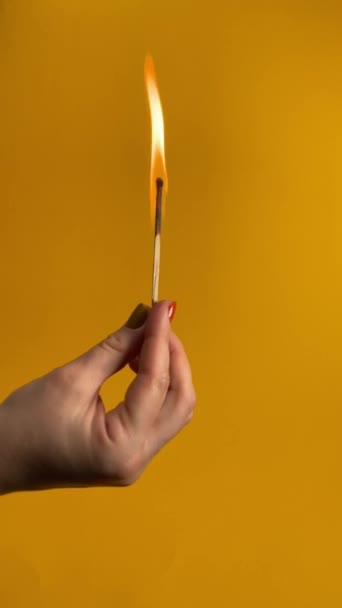 无法辨认的女性手持一根燃烧的火柴 轻轻吹灭了火焰 并在橙色的背景上暴露了逐渐消逝的烟雾 室内垂直工作室拍摄 耗竭的抽象概念 — 图库视频影像