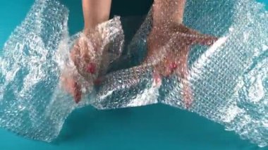 Plastik kirliliğine dair soyut bir anlam taşıyan bir kinaye. Paketleme konsepti. Tanımlanamayan kadın elleri baloncuklu bir baloncuğa sarılmış. Mavi arka planda izole edilmiş kapalı stüdyo görüntüleri.