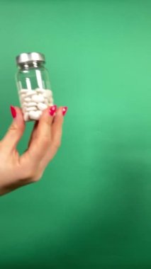 Beslenme takviyesi fikri. Tanınmayan bir kadın bir şişe vitamin ya da hap sergiliyor ve elinde çeviriyor. Yeşil arkaplanda dikey çekim izole edildi. Sağlık ve Sıhhat kavramı