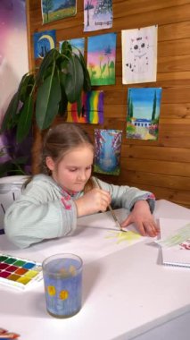 Gençlik sanatsal ifadeleri, çocukluk hobileri. Tatlı küçük bir kızın dikey hali suluboya resim yapıyor, yaratıcılığını ve hayal gücünü kapalı alandaki çizimler ve ev bitkileriyle keşfediyor.