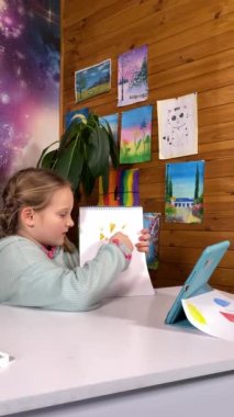 Yaratıcı yayıncılık, çocukluk hobisi. Küçük çocuk blogcuların dikey hali, içerideki dijital tablet hakkında ipuçları çiziyor. Resimlerin ve ev bitkilerinin arkaplanındaki çocuklar için ilham verici çevrimiçi sanat kanalı