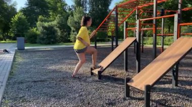 Açık hava fitness eğitim alanında fiziksel aktivite. Çok ırklı genç bir kadın güneş doğarken halka açık bir parkta sabah antrenmanına çıkıyor. Güç, esneklik, refah kavramı