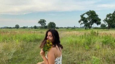 Eğlence, boş zaman, açık hava. Çok ırklı elbiseli çekici bir genç kadın doğanın güzelliğine hayran, çayırlarda geziniyor, yaz mevsiminde çimenlerin ve kır çiçeklerinin tadını çıkarıyor.