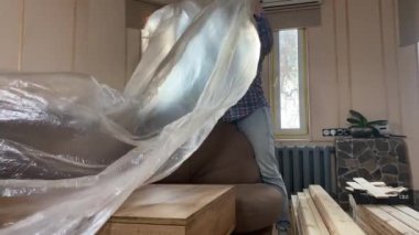 Evde tadilat yapan bir kadın, içerideki inşaat malzemelerinin yenilenmesi için hazırlık yapıyor. Yeniden yapılanma, DIY konsepti. Temizlikçi kadın mobilya koruması kullanıyor.