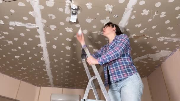 一名妇女在室内修理天花板的背景下从事住房装修和翻新工作 Diy概念 女服务员在灯具中更换灯泡 固定电灯 — 图库视频影像