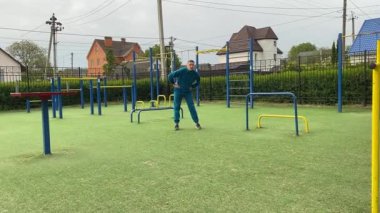Odaklanmış genç bir atlet dinamik bir şekilde ısınma egzersizleri yapıyor ve dışarıda esniyor. Atletizm kıyafetlerini giyip titizlikle vücudu düzenli bir rutine göre fiziksel taleplere hazırlıyor.