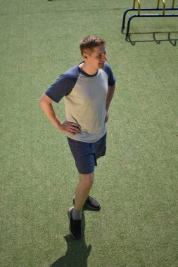 Odaklanmış genç bir atlet dinamik bir şekilde ısınma egzersizleri yapıyor ve dışarıda esniyor. Atletizm kıyafetlerini giyip titizlikle vücudu düzenli bir rutine göre fiziksel taleplere hazırlıyor.