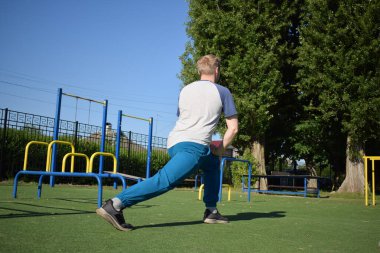 Odaklanmış genç bir atlet dinamik bir şekilde ısınma egzersizleri yapıyor ve dışarıda esniyor. Atletizm kıyafetlerini giyip titizlikle vücudu düzenli bir rutine göre fiziksel taleplere hazırlıyor.