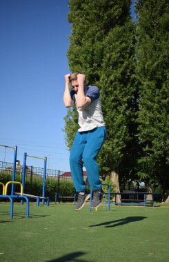 Odaklanmış genç bir atlet dinamik bir şekilde ısınma egzersizleri yapıyor ve dışarıda esniyor. Atletizm kıyafetlerini giyip titizlikle vücudu düzenli bir rutine göre fiziksel taleplere hazırlıyor.