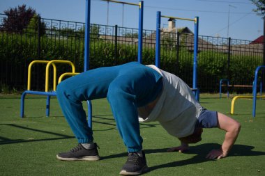 Odaklanmış genç bir atlet dinamik bir şekilde ısınma egzersizleri yapıyor ve dışarıda esniyor. Atletizm kıyafetlerini giyip titizlikle vücudu düzenli bir rutine göre fiziksel taleplere hazırlıyor.