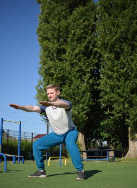 Odaklanmış genç bir atlet dinamik bir şekilde ısınma egzersizleri yapıyor ve dışarıda esniyor. Atletizm kıyafetlerini giyip titizlikle vücudu düzenli bir rutine göre fiziksel taleplere hazırlıyor.