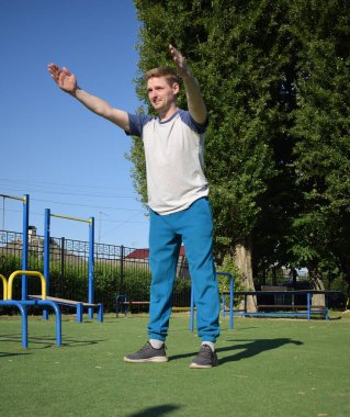 Odaklanmış genç bir atlet dinamik bir şekilde ısınma egzersizleri yapıyor ve dışarıda esniyor. Atletizm kıyafetlerini giyip titizlikle vücudu düzenli bir rutine göre fiziksel taleplere hazırlıyor.