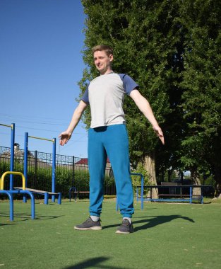 Odaklanmış genç bir atlet dinamik bir şekilde ısınma egzersizleri yapıyor ve dışarıda esniyor. Atletizm kıyafetlerini giyip titizlikle vücudu düzenli bir rutine göre fiziksel taleplere hazırlıyor.