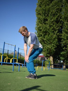 Odaklanmış genç bir atlet dinamik bir şekilde ısınma egzersizleri yapıyor ve dışarıda esniyor. Atletizm kıyafetlerini giyip titizlikle vücudu düzenli bir rutine göre fiziksel taleplere hazırlıyor.