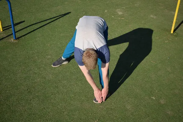 stock image A focused young athlete dynamically performing warm-up drills and stretches outdoors. Clad in athletic gear, he meticulously prepares body for the physical demands ahead through a regimented routine