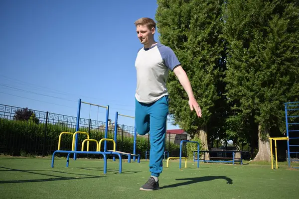 stock image A focused young athlete dynamically performing warm-up drills and stretches outdoors. Clad in athletic gear, he meticulously prepares body for the physical demands ahead through a regimented routine