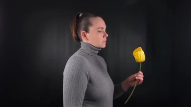 Güzel bir genç kadının portresi narin bir çiçek tutar, güzel bir yüz ifadesiyle güzel kokulu bir koku kokar. Siyah bir arka planda gri bir kazak giyiyor, zahmetsiz bir serinlik yayıyor.