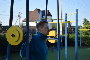 A dedicated young athlete puts in the hard work, vigorously training on gym equipment outdoors to prepare his body. He builds strength and endurance before hitting the field or court for competition