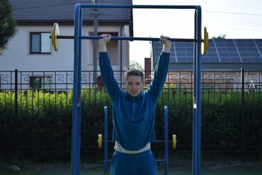 A dedicated young athlete puts in the hard work, vigorously training on gym equipment outdoors to prepare his body. He builds strength and endurance before hitting the field or court for competition