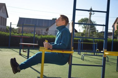 A dedicated young athlete puts in the hard work, vigorously training on gym equipment outdoors to prepare his body. He builds strength and endurance before hitting the field or court for competition