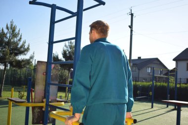 A dedicated young athlete puts in the hard work, vigorously training on gym equipment outdoors to prepare his body. He builds strength and endurance before hitting the field or court for competition