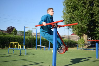A dedicated young athlete puts in the hard work, vigorously training on gym equipment outdoors to prepare his body. He builds strength and endurance before hitting the field or court for competition