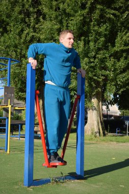 A dedicated young athlete puts in the hard work, vigorously training on gym equipment outdoors to prepare his body. He builds strength and endurance before hitting the field or court for competition