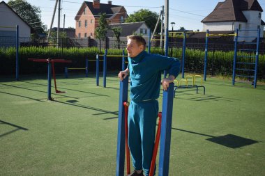 A dedicated young athlete puts in the hard work, vigorously training on gym equipment outdoors to prepare his body. He builds strength and endurance before hitting the field or court for competition
