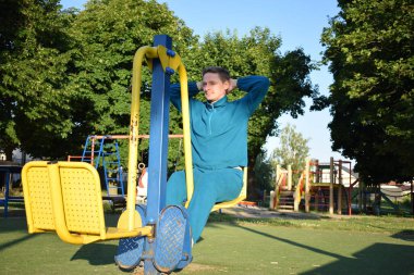 A dedicated young athlete puts in the hard work, vigorously training on gym equipment outdoors to prepare his body. He builds strength and endurance before hitting the field or court for competition