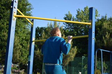 A dedicated young athlete puts in the hard work, vigorously training on gym equipment outdoors to prepare his body. He builds strength and endurance before hitting the field or court for competition