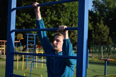 A dedicated young athlete puts in the hard work, vigorously training on gym equipment outdoors to prepare his body. He builds strength and endurance before hitting the field or court for competition