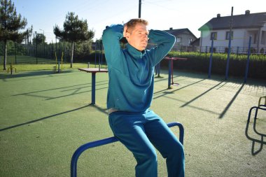 A dedicated young athlete puts in the hard work, vigorously training on gym equipment outdoors to prepare his body. He builds strength and endurance before hitting the field or court for competition
