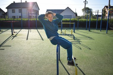A dedicated young athlete puts in the hard work, vigorously training on gym equipment outdoors to prepare his body. He builds strength and endurance before hitting the field or court for competition