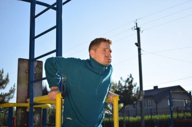A dedicated young athlete puts in the hard work, vigorously training on gym equipment outdoors to prepare his body. He builds strength and endurance before hitting the field or court for competition