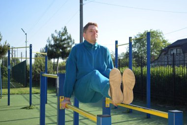 A dedicated young athlete puts in the hard work, vigorously training on gym equipment outdoors to prepare his body. He builds strength and endurance before hitting the field or court for competition