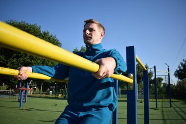 A dedicated young athlete puts in the hard work, vigorously training on gym equipment outdoors to prepare his body. He builds strength and endurance before hitting the field or court for competition