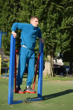 A dedicated young athlete puts in the hard work, vigorously training on gym equipment outdoors to prepare his body. He builds strength and endurance before hitting the field or court for competition
