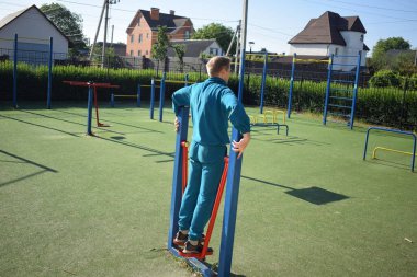 A dedicated young athlete puts in the hard work, vigorously training on gym equipment outdoors to prepare his body. He builds strength and endurance before hitting the field or court for competition