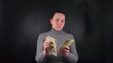 Gösterişli genç bir kadın hevesle bir tomar para sayıyor. Basit bir siyah fon üzerinde hayat değiştiren bir şans vuruşunun heyecanı. Kutlama sevincinin simgesi.