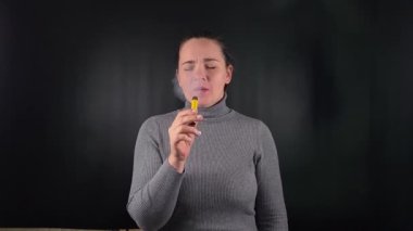 E- sigara içen, siyah arka planda öksüren genç bir kadının portresi. Zararlı etkiler ve sigarayla ilişkili riskler, minimalist bir ortamda kötü bir alışkanlıkla mücadele