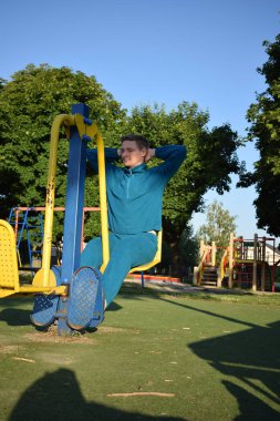 A dedicated young athlete puts in the hard work, vigorously training on gym equipment outdoors to prepare his body. He builds strength and endurance before hitting the field or court for competition