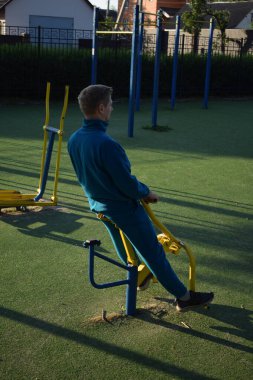A dedicated young athlete puts in the hard work, vigorously training on gym equipment outdoors to prepare his body. He builds strength and endurance before hitting the field or court for competition