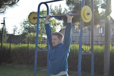 A dedicated young athlete puts in the hard work, vigorously training on gym equipment outdoors to prepare his body. He builds strength and endurance before hitting the field or court for competition