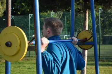 A dedicated young athlete puts in the hard work, vigorously training on gym equipment outdoors to prepare his body. He builds strength and endurance before hitting the field or court for competition